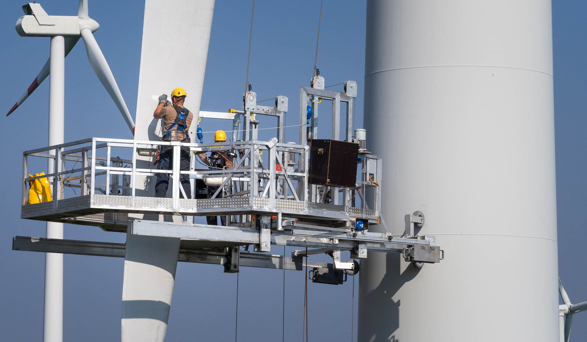 Workers on a hanging platform repair a damaged rotor blade on a