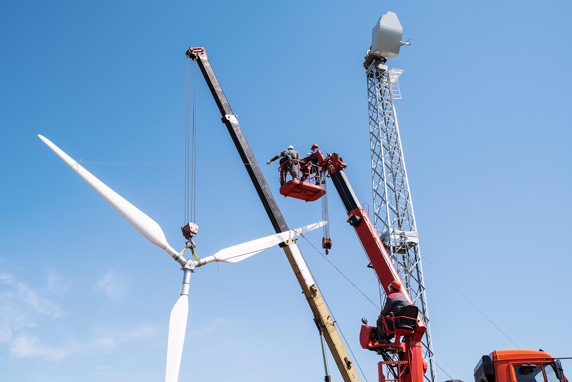 Construction of a wind power plant. Installers use a truck crane and aerial platform to raise the wind turbine rotor.