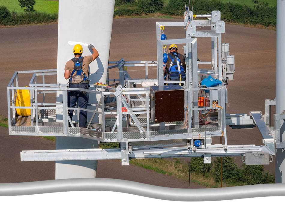 Two workers in full safety gear, up on platforms/ man baskets, doing maintenance on a wind turbine blade.