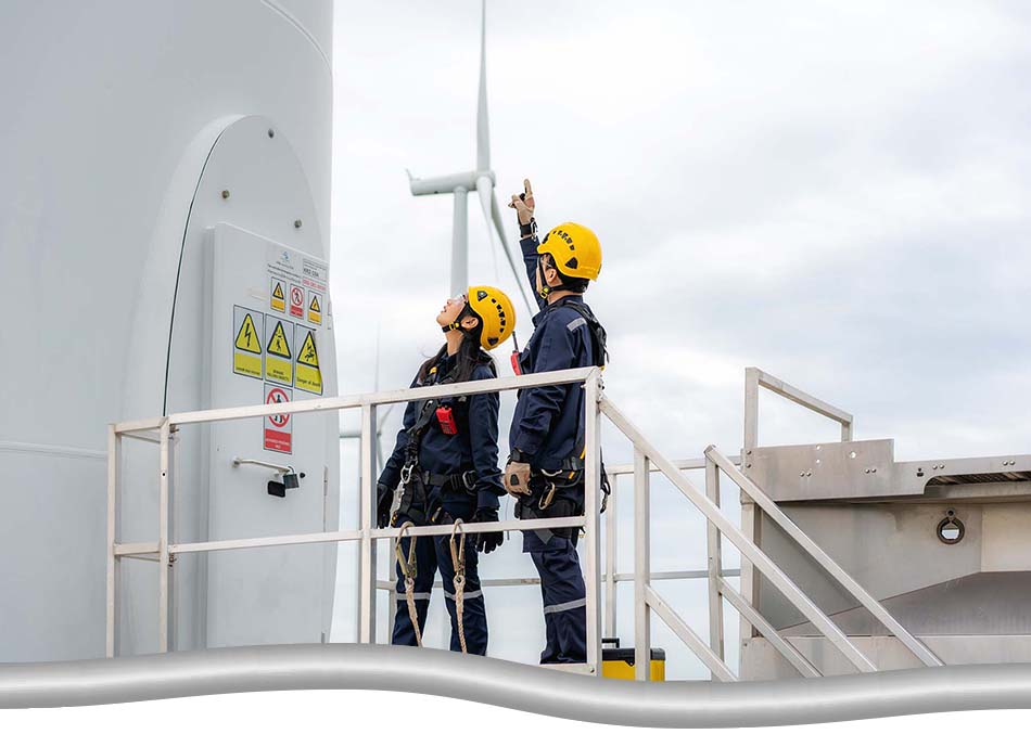 Instructor and trainee safety training on site by a wind turbine, in full safety gear, and safety hooks attached to the railing.