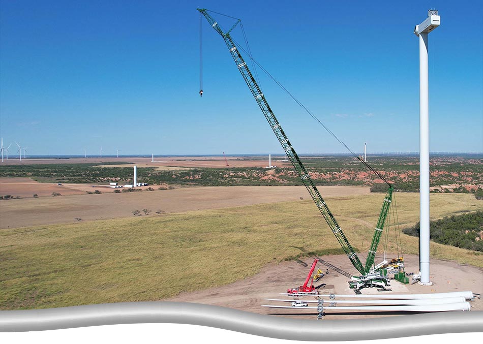 large green crane with smaller red support crane, next to a wind turbine, mid construction.